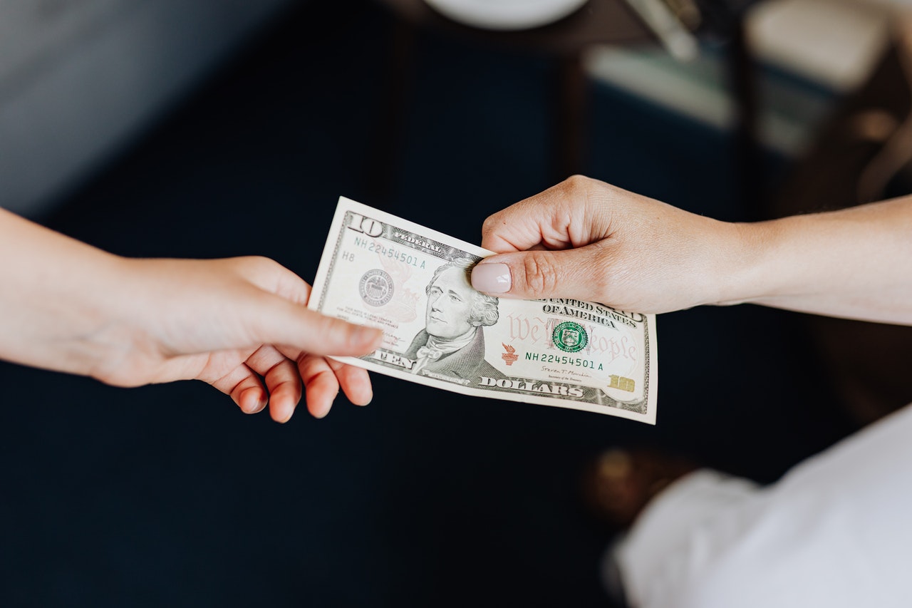 Close-up of two hands exchanging a ten-dollar bill against a dark blurred background in a neutral indoor setting